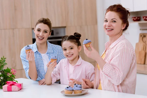 Tres generaciones de mujeres comiendo cupcakes en la cocina - foto de stock