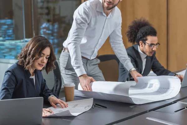 Team of young architects working with building plans at conference hall of office — Stock Photo