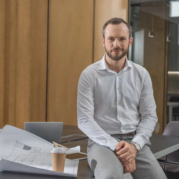 Handsome architect sitting on table with plans at office — Stock Photo