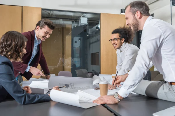 Grupo de arquitectos sonrientes trabajando juntos en la construcción de planos en la oficina - foto de stock