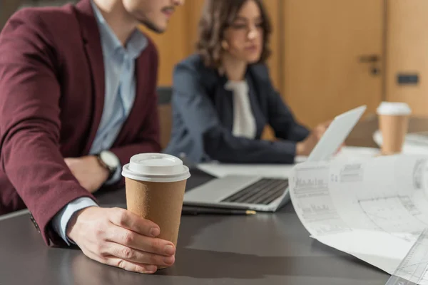 Recortado tiro de los empresarios con tazas de papel de café trabajando con el ordenador portátil juntos en la oficina - foto de stock