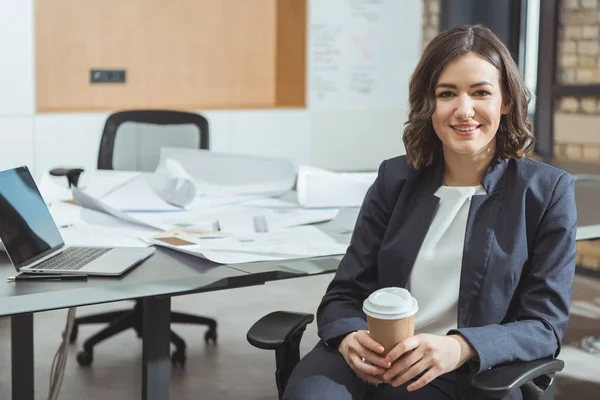 Beautiful young architect with coffee to go in front of workplace — Stock Photo