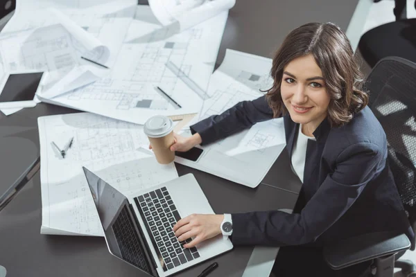 Vista de ángulo alto del hermoso arquitecto joven con café para ir a trabajar con el ordenador portátil - foto de stock