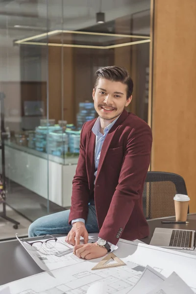 Beau jeune architec assis sur le bureau et regardant la caméra au bureau — Photo de stock