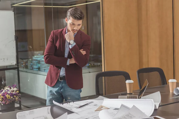 Jeune architecte réfléchi regardant les plans de construction au bureau — Photo de stock