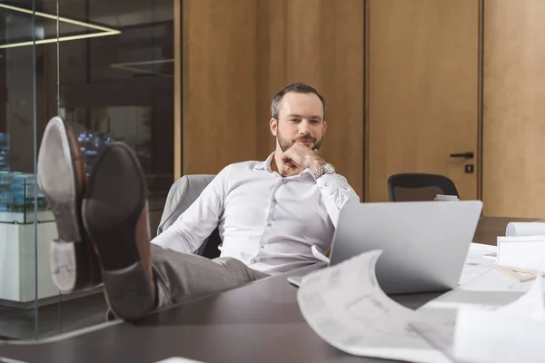 Schöner nachdenklicher Architekt sitzt am Arbeitsplatz und schaut auf Laptop — Stockfoto