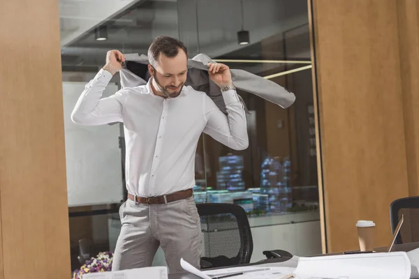 Handsome architect putting on suit and looking at plans at office — Stock Photo