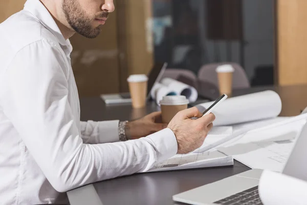Handsome architect with paper cup of coffee using smartphone at office — Stock Photo