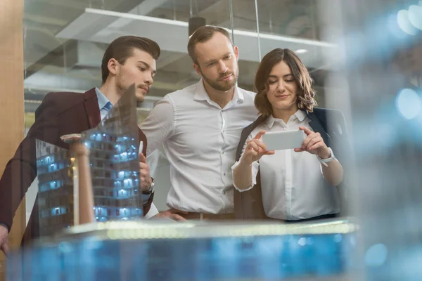 Team of architects taking photo of miniature town model with smartphone — Stock Photo