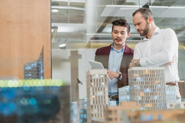 Thoughtful architects with tablet in front of building models — Stock Photo