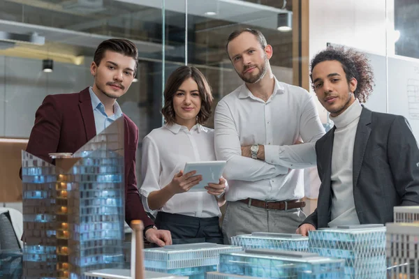 Grupo de arquitectos exitosos de pie junto a los modelos de construcción en la oficina - foto de stock