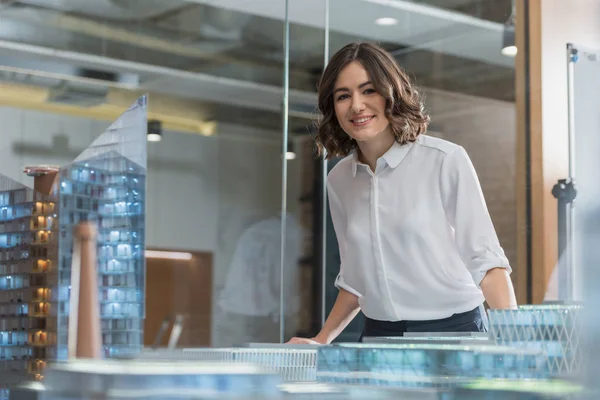 Beautiful young architect standing near building models — Stock Photo