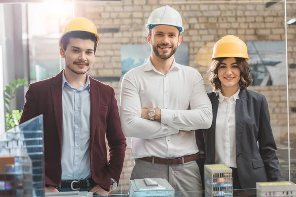 Equipe de arquitetos em chapéus duros na frente do modelo de cidade em miniatura no escritório — Fotografia de Stock