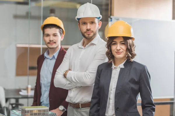 Equipo de arquitectos exitosos en sombreros duros frente al modelo de ciudad en miniatura - foto de stock