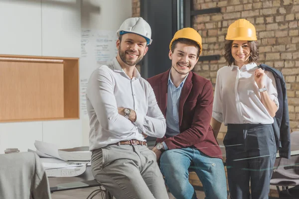 Team of successful architects in hard hats looking at camera — Stock Photo