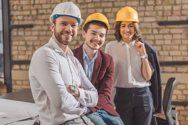 Team glücklicher Architekten mit harten Hüten blickt in die Kamera — Stockfoto