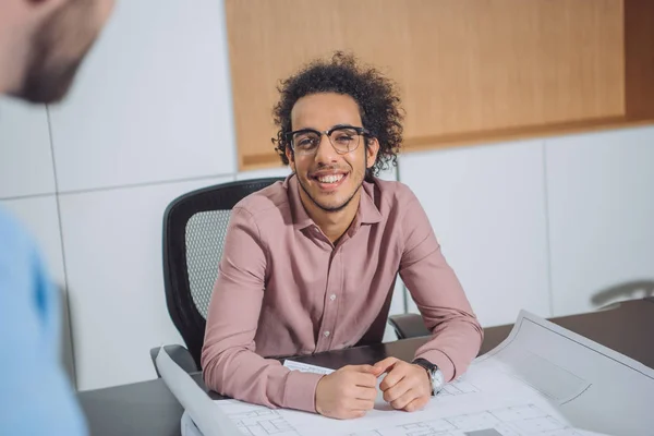 Apuesto joven arquitecto con plan de construcción hablando con su colega en la oficina - foto de stock