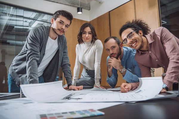 Group of successful architects discussing plans and looking at camera at office — Stock Photo