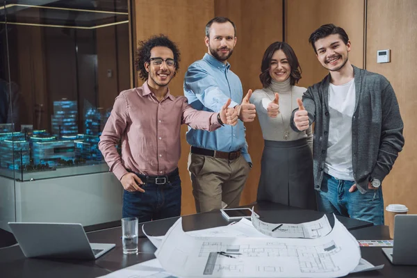 Grupo de arquitectos exitosos mostrando pulgares hacia arriba en la oficina - foto de stock