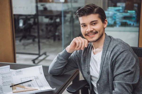 Schöner junger Architekt sitzt am Arbeitsplatz mit Bauplänen im Büro — Stockfoto