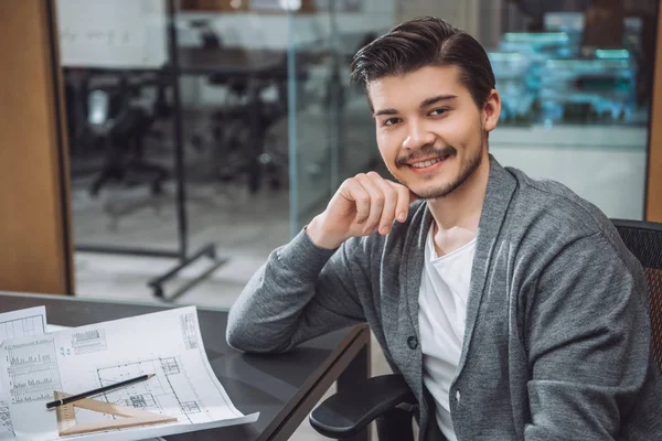 Beau jeune architecte assis sur le lieu de travail avec des plans de construction au bureau — Photo de stock