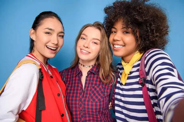 Smiling multiethnic students taking selfie, isolated on blue — Stock Photo