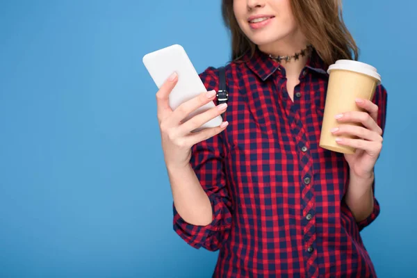 Vista cortada de menina com café para ir usando smartphone, isolado em azul — Fotografia de Stock