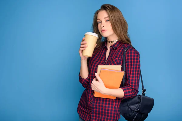 Jovem estudante do sexo feminino em pé com livros e café para ir, isolado em azul — Fotografia de Stock