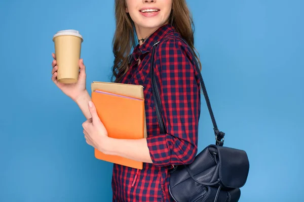 Vista cortada de jovem estudante de pé com mochila, livros e café para ir, isolado em azul — Fotografia de Stock