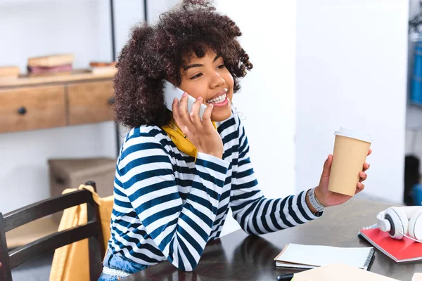 Smiling african american student with coffee to go talking on smartphone — Stock Photo
