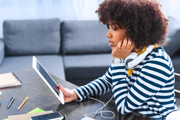 Vista laterale dello studente afroamericano con cuffie e tablet seduto a tavola — Foto stock