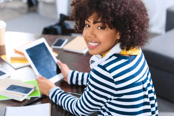 Étudiant afro-américain souriant avec écouteurs et tablette assis à la table — Photo de stock