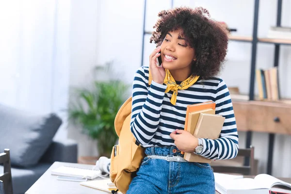 Ritratto di uno studente afroamericano sorridente con libri che parlano su smartphone — Foto stock