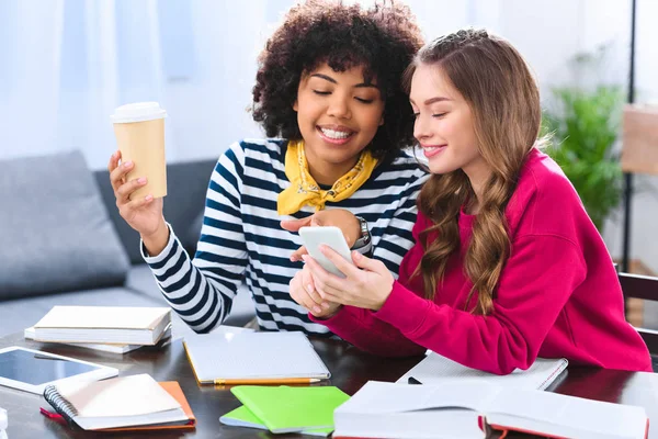 Улыбающиеся мультикультурные студенты, использующие смартфон во время учебы вместе — стоковое фото