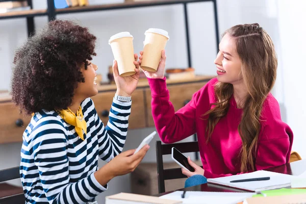 Estudiantes multiculturales tintinear tazas de café desechables mientras estudian juntos - foto de stock
