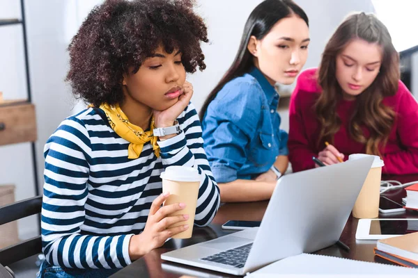 Selective focus of bored african american young woman with laptop and multicultural students near by — Stock Photo