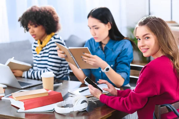 Foyer sélectif de sourire jeune femme avec smartphone et étudiants multiethniques à proximité — Photo de stock