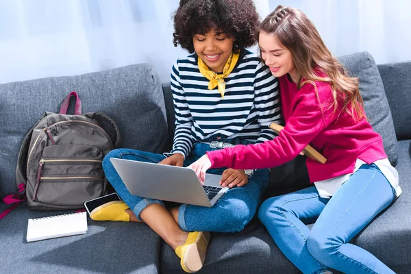 Estudiantes multiculturales sonrientes usando el ordenador portátil mientras estudian juntos - foto de stock