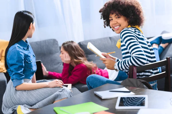 Selektiver Fokus eines lächelnden afrikanisch-amerikanischen Studenten, der in die Kamera schaut, während multirassische Freunde Laptop benutzen — Stockfoto