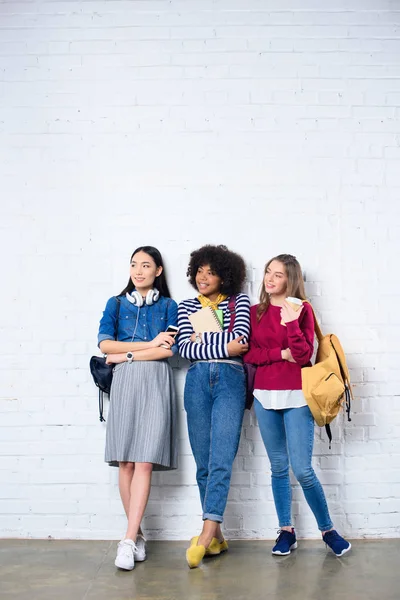 Junge multiethnische Studenten stehen vor weißer Backsteinmauer — Stockfoto