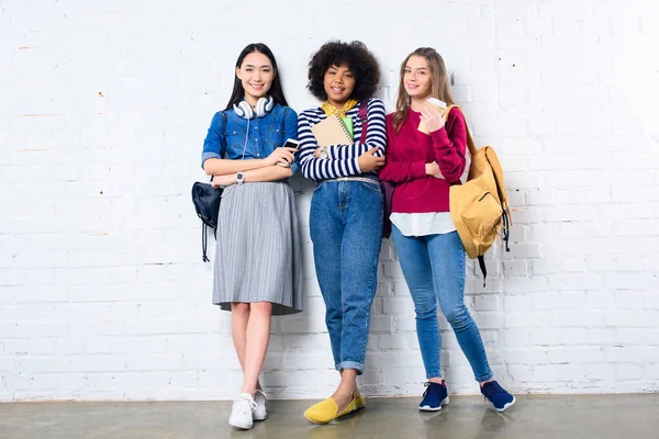 Étudiants souriants multiraciaux debout contre le mur de briques blanches — Photo de stock