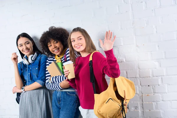 Retrato de sorrir estudantes multirraciais em pé contra parede de tijolo branco — Fotografia de Stock