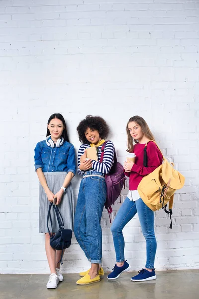 Young multiracial students standing against white brick wall — Stock Photo