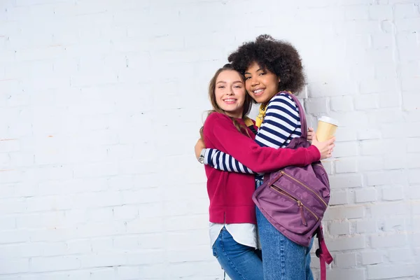 Porträt fröhlicher multikultureller Studenten, die sich an einer weißen Backsteinwand umarmen — Stockfoto