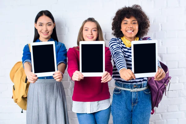 Multicultural students showing tablets with blank screens in hands against white brick wall — Stock Photo