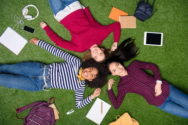Над головой вид веселых мультикультурных студентов, лежащих на зеленой лужайке — стоковое фото