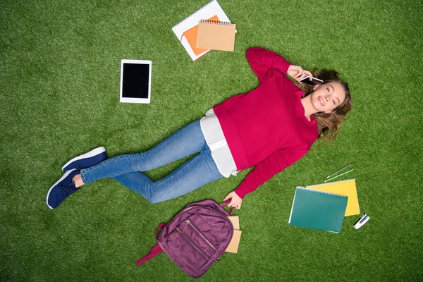 Blick von oben auf junge Studentin, die auf grünem Rasen auf dem Smartphone spricht — Stockfoto