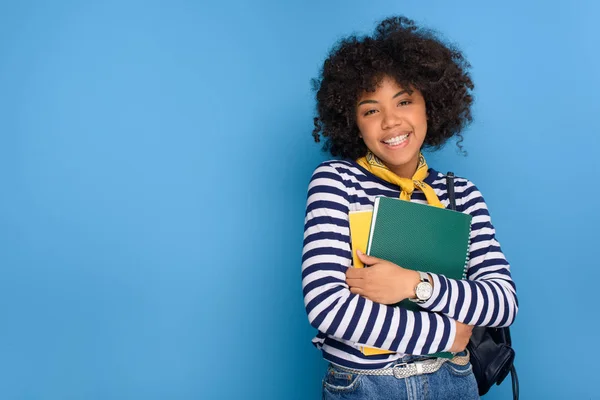 Portrait of cheerful african american student with notebooks isolated on blue — Stock Photo