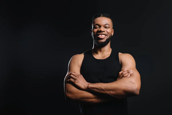 Bonito sorridente jovem Africano americano desportista de pé com cruzados braços isolado no preto — Fotografia de Stock