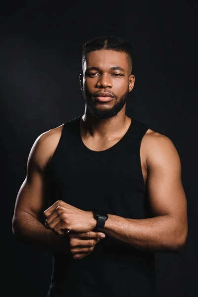 Young african american sportsman using smartwatch and looking at camera isolated on black — Stock Photo